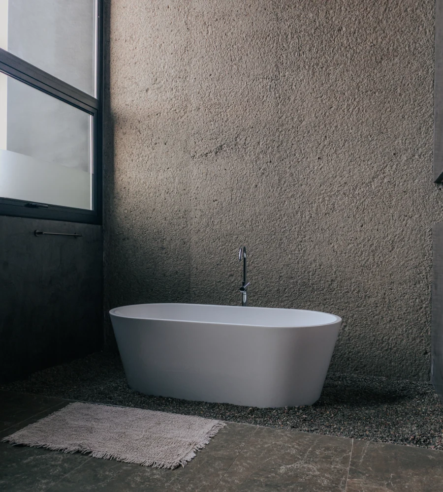 Oval white bathtub in a modern bathroom with gray textured wall